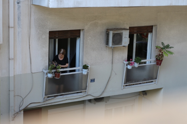 woman watering plants out window in greece, athens